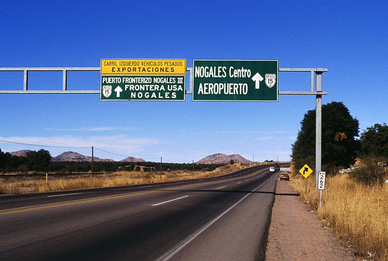 <i>Near the Mex. 15D split just south of Nogales.  As the sign says, one branch goes to downtown Nogales (and the border crossing near where I-19 begins), while the other heads out west to what is called Nogales III on the Mexican side and Mariposa on the US side.  The Mexican immigration and Customs station is actually a substantial distance south of the border and the length of the Mex. 15D expressway between the border and the border station is a closed "corredor fiscal," with high chain-link fences designed to prevent entry and exit.  The fences do not stop trinket sellers, however.  </i>