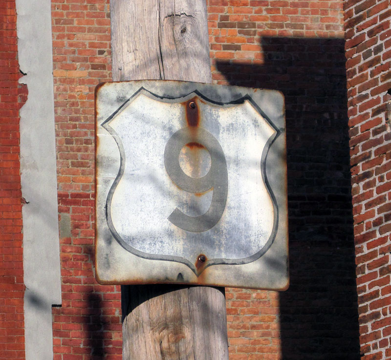 This shield was originally a white square with the outline shield, and then got repainted to a black square around 1961. The repaint is clearly fading.